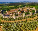 Borgo medievale fortificato su una collina, circondato da uliveti e vigneti. Bellissimi paesaggi toscani sotto un cielo azzurro.