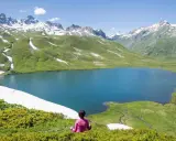 Pace e natura in Valle d'Aosta in estate: un lago alpino azzurro circondato da montagne innevate e verdi pascoli.
