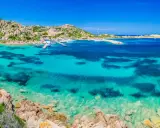 Acque cristalline e rocce granitiche ti aspettano per una visita alla Maddalena. Un paradiso azzurro con barche all'ancora.