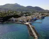 Ischia vista da Napoli: un borgo colorato si affaccia sul mare blu, con montagne verdi sullo sfondo.