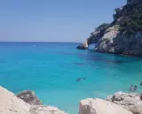 Acqua cristallina e scogliere a picco a Cala Goloritzè, raggiungibile con un suggestivo **percorso a piedi**. Persone nuotano e si rilassano.
