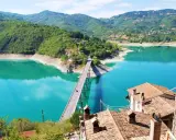 Panoramica mozzafiato del lago turchese vicino a Castel di Tora, con un ponte che attraversa le acque cristalline e montagne verdi sullo sfondo.
