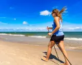 Donna con bastoncini da nordic walking in una splendida passeggiata al mare, con il vento che le scompiglia i capelli.