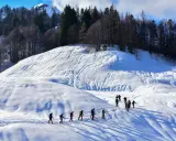 Un gruppo di escursionisti fa **passeggiate sulla neve** in un paesaggio montano innevato, con alberi scuri sullo sfondo.