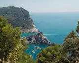 Vista panoramica del sentiero Riomaggiore Portovenere, con la chiesa di San Pietro su uno sperone roccioso e il mare azzurro.