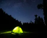 Tenda illuminata nella notte stellata, un invito a dormire in tenda immersi nella natura.