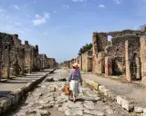 Una donna con cappello di paglia cammina lungo una strada lastricata di Pompei, tra antiche rovine. Un'esperienza unica per scoprire cosa vedere a Pompei.