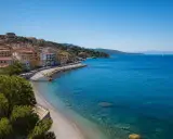 Porto Santo Stefano: case colorate affacciate su spiagge di ciottoli e sabbia, con il mare azzurro e un veliero all'orizzonte.