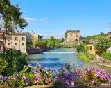 Un fiume attraversa un pittoresco borgo medievale veneto, con un'antica torre in rovina e case colorate.