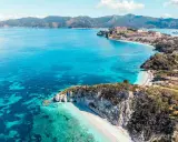 Costa rocciosa con spiaggia bianca e mare cristallino, un borgo fortificato domina la baia. Splendida località mare Toscana.