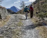 Escursionisti su sentiero sassoso nel Val di Susa, con montagne sullo sfondo.