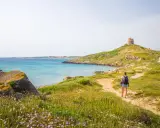 Sentiero panoramico per un tour Sardegna 7 giorni, con torre antica e mare turchese.