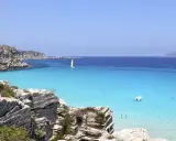 Scogliere rocciose e mare cristallino a Favignana. Un veliero solca le acque turchesi, perfetto per scoprire cosa vedere a Favignana in un giorno.