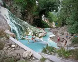Cascata bianca e pozze azzurre alle terme San Filippo, con persone che si rilassano nell'acqua termale.