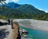 Ciclovia del Tagliamento: due ciclisti esplorano il sentiero panoramico lungo il fiume, circondati da montagne verdi e un cielo azzurro.