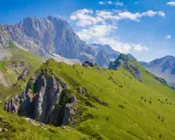 Prati verdi e sentieri invitano a **passeggiate facili** in Val Seriana, con maestose cime sullo sfondo sotto un cielo azzurro.