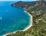 Baia con acque cristalline e numerose barche, incastonata tra colline verdi e scogliere. Un vero gioiello tra le spiagge più belle Toscana.