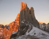 Le Torri del Vajolet illuminate dal caldo bagliore del tramonto, con la neve che ricopre le cime rocciose.