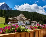 Fiori colorati su un balcone con vista su un hotel e le montagne, un'oasi di pace nei rifugi Val Gardena.