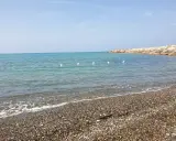 Spiagge più belle della Marina di Cecina: mare azzurro, ciottoli levigati e un molo roccioso con qualche bagnante.