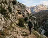 Escursionista su un sentiero dello spirito, con un antico eremo incastonato nella roccia e montagne sullo sfondo.