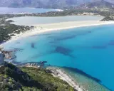 Torre costiera su promontorio verdeggiante domina una baia con acque cristalline, tra le spiagge più belle Sardegna.