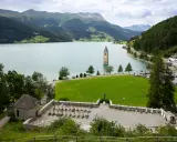Un antico campanile nel lago, circondato da montagne verdi e un cimitero.