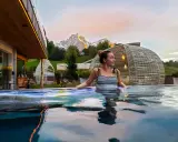 Donna rilassata in una piscina a sfioro con vista sulle montagne illuminate al tramonto, un'esperienza di benessere nelle terme in Trentino Alto Adige.