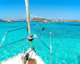 La prua di una barca a vela naviga verso La Maddalena, tra acque cristalline e isole rocciose.