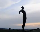 Statua silhouette con braccia aperte, su un crinale collinare, al tramonto. Un punto panoramico lungo le tappe della Via Romea Sanese.