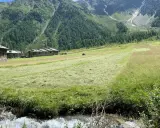 Case in pietra nel **Val di Rezzalo**, prati falciati e un ruscello che scorre ai piedi di montagne verdi e rocciose.