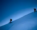 Due escursionisti con ciaspole salgono un pendio innevato sotto un cielo blu intenso. Le ciaspole sono perfette per camminare sulla neve fresca.