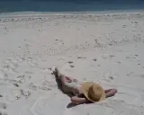 Persona distesa su sabbia bianca, con cappello di paglia, vicino al mare turchese. Un'immagine che evoca la pace delle spiagge naturiste in Italia.