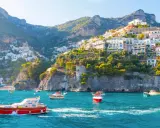 Barche a vela navigano nelle acque turchesi davanti alle case colorate aggrappate alle scogliere delle isole costiera amalfitana.