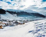 Paesaggio invernale con villaggio innevato e montagne sullo sfondo. Perfetto per sapere dove andare in montagna in Trentino per sciare.