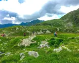 Escursionisti attraversano un paesaggio verdeggiante in una località montagna Piemonte, con rocce e nuvole minacciose all'orizzonte.