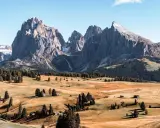 Un paesaggio mozzafiato delle Dolomiti più belle, con cime imponenti, prati dorati e boschi verdi. Piccole baite sparse creano un'atmosfera idilliaca.