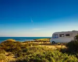 Un camper bianco sosta su un sentiero sabbioso con vista sul mare blu intenso. Un'avventura indimenticabile in camper all'Isola d'Elba.
