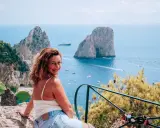 Donna sorridente con vista sui Faraglioni, un'ispirazione per come visitare Capri. Mare azzurro e barche in lontananza.