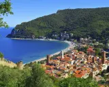 Vista panoramica di pittoreschi liguria paesi sul mare, con case dai tetti rossi che scendono verso una baia azzurra e una spiaggia affollata.