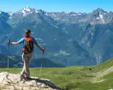 Escursionista con zaino e bastoncini ammira un panorama alpino mozzafiato, perfetto per scoprire gli itinerari della Valle d'Aosta.