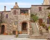 Antica piazza con case in pietra, scale in terracotta e piante rigogliose, un'atmosfera da **borghi medievali toscana**.