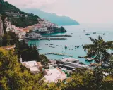 Vista panoramica di un villaggio colorato sulla Costiera Amalfitana, con barche nel porto e montagne sullo sfondo. Un invito a scoprire come visitare la Costiera Amalfitana.