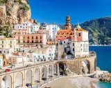Un incantevole borgo da visitare in Campania, con case colorate aggrappate alla roccia, un ponte ad archi e il mare blu.