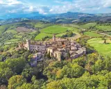 Un borgo medievale arroccato su una collina, circondato da dolci colline verdi. Un esempio dei borghi più belli della Toscana.