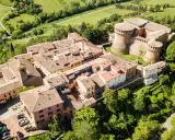 Aerial view of a medieval Italian village with a castle, terracotta roofs, and surrounding green hills.