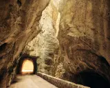 La strada della forra si snoda tra imponenti pareti rocciose, con un tunnel che si apre verso una luce accecante.
