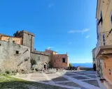 Piazza nel centro storico di Borgio Verezzi con edifici antichi, tavolini all'aperto e il mare sullo sfondo.