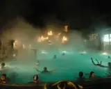 Persone si rilassano in una piscina termale notturna, con luci natalizie che brillano tra la nebbia, un'atmosfera magica nei bagni di Romagna.