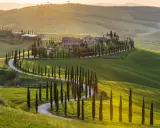 Colline toscane al tramonto, cipressi lungo una strada tortuosa, un casale in pietra. Ecco cosa vedere in Val d'Orcia.